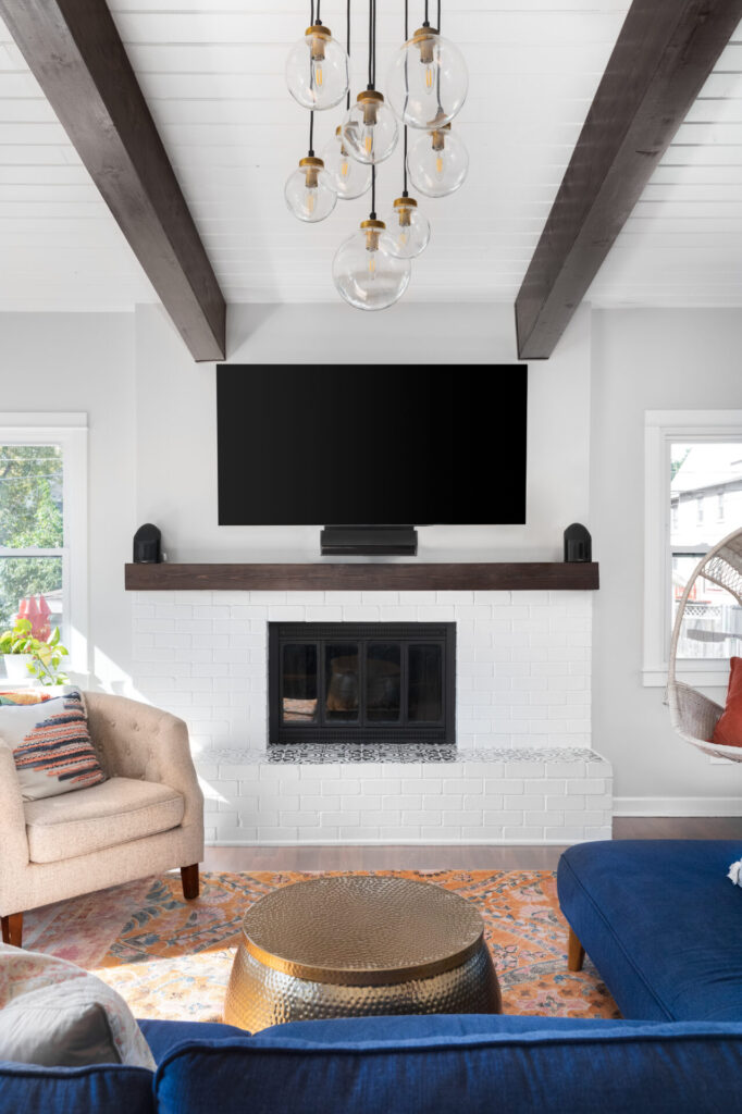 A farmhouse living room with a television over a fireplace and chandelier hanging from the shiplap ceiling.